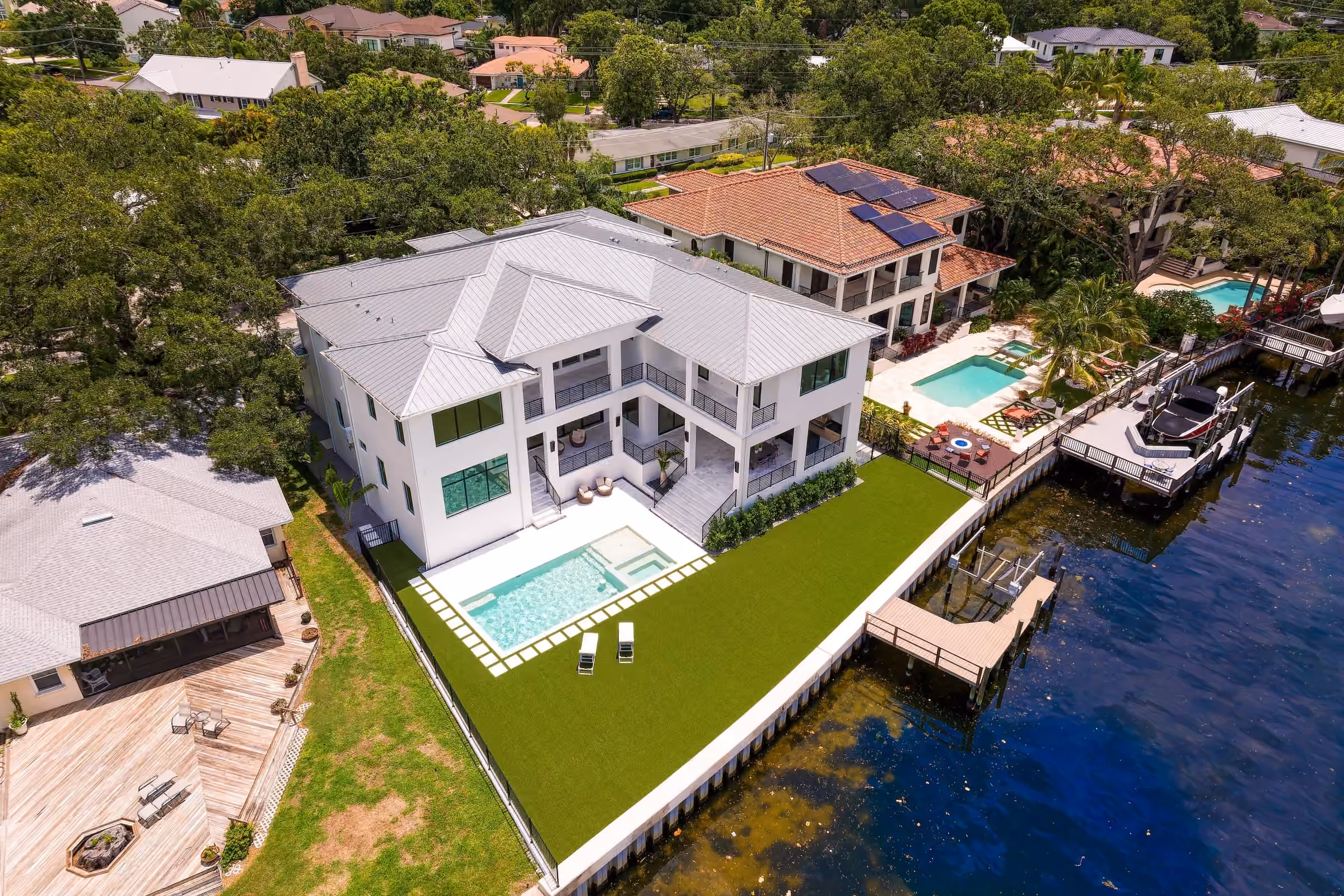 Aerial view of a two-story white home with a pool on a canal