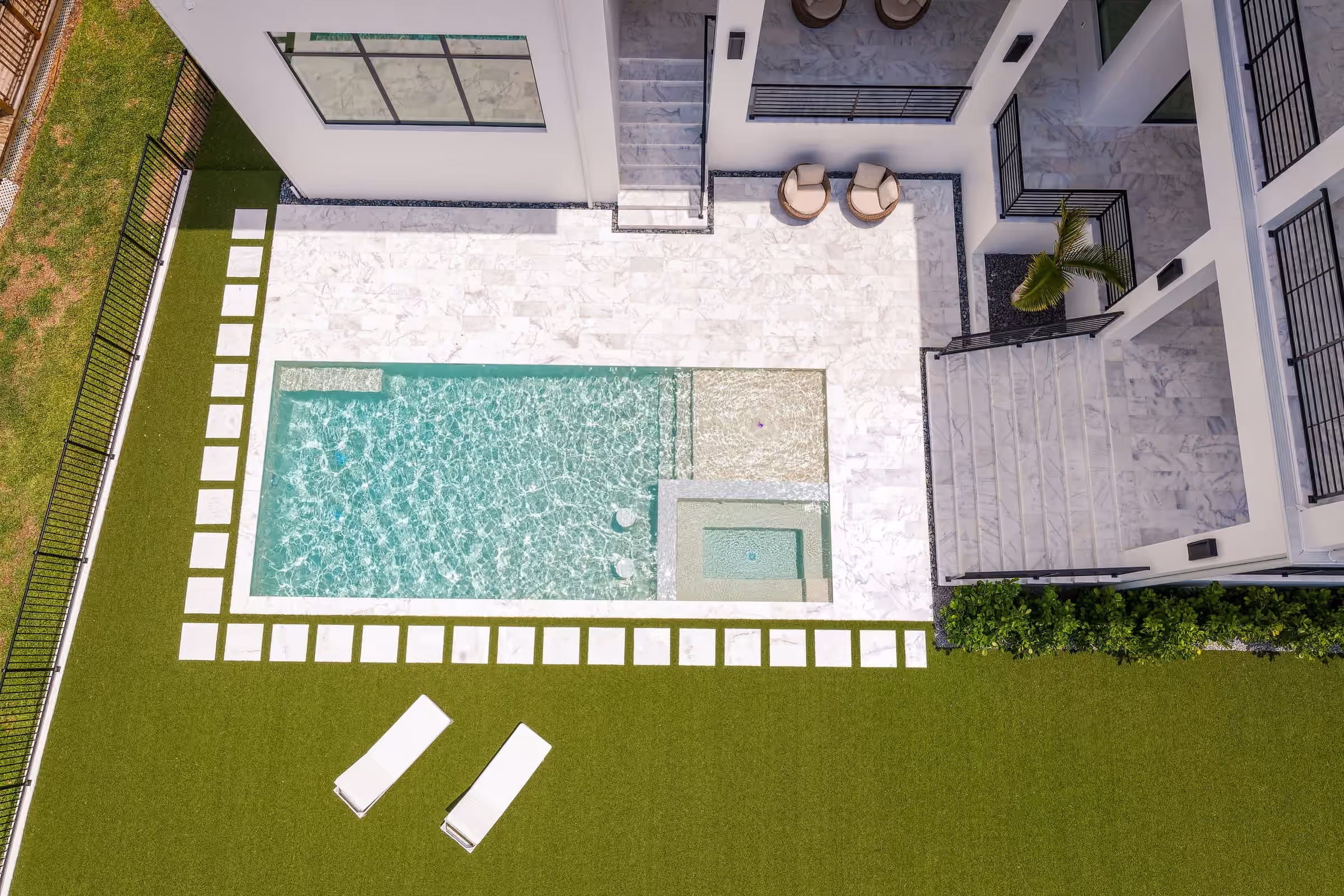 Aerial view of a pool courtyard with a turf lawn and lounge chairs behind a Halo home