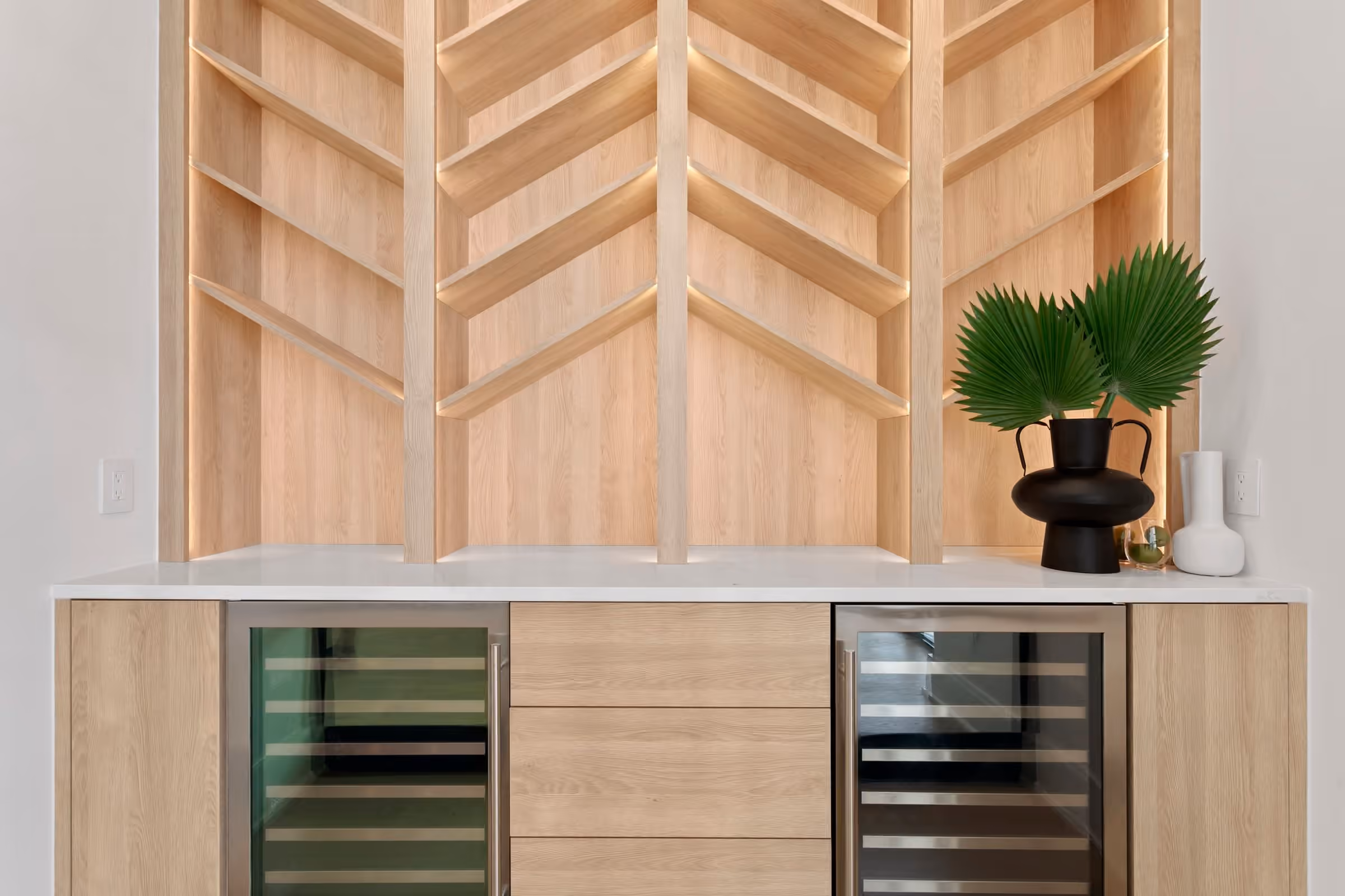 Built-in bar with light oak chevron shelving and two wine fridges