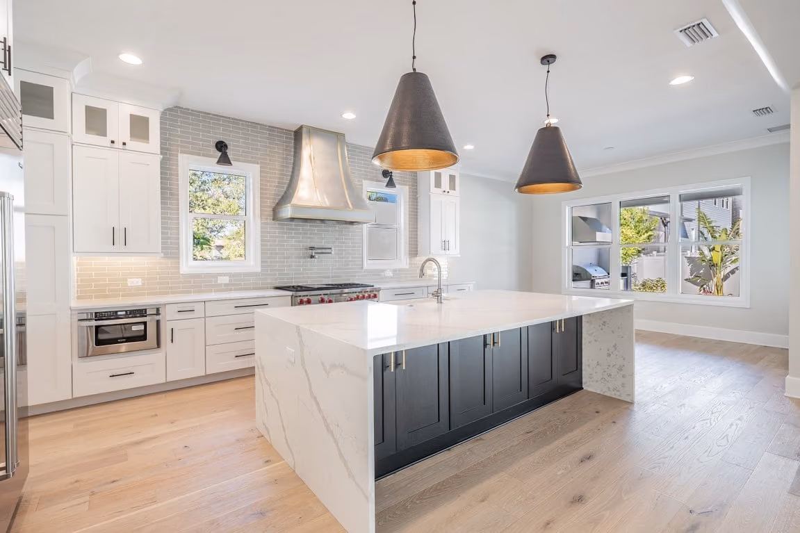 Kitchen with white cabinets, a waterfall island with a dark base and pendant lights