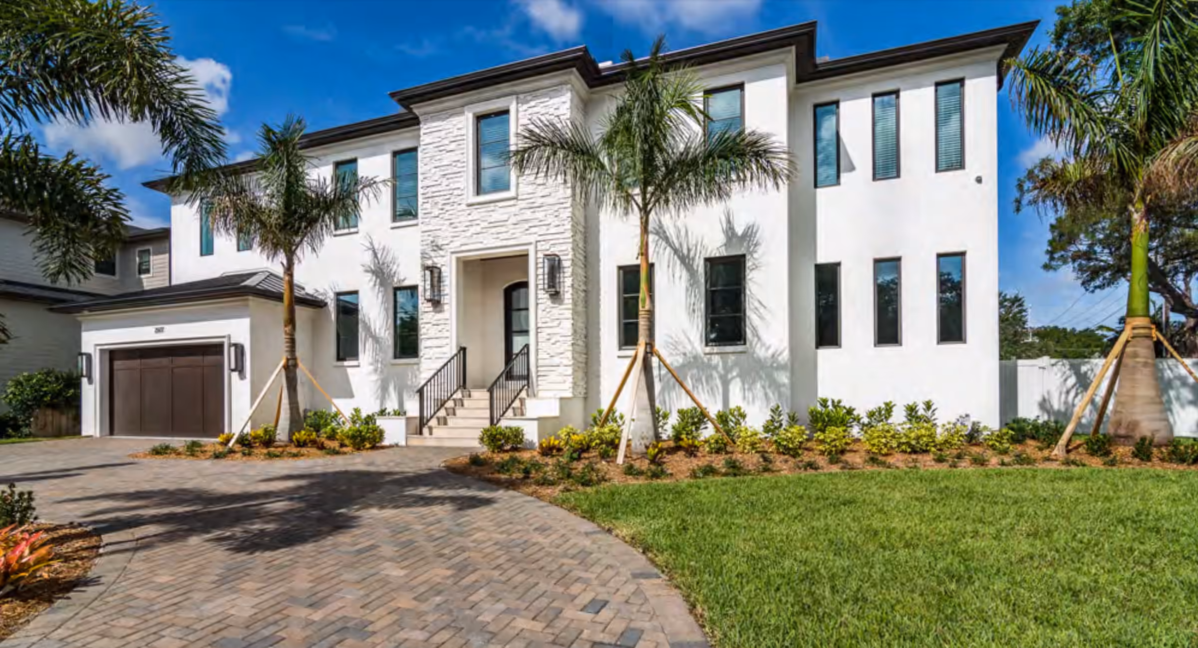 Two-story white home with stone cladding, palms and a paver drive