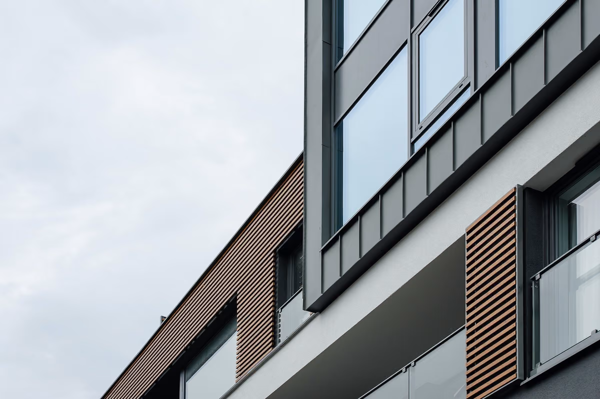 Close view of a modern exterior with wood slats, dark panels and a glass railing