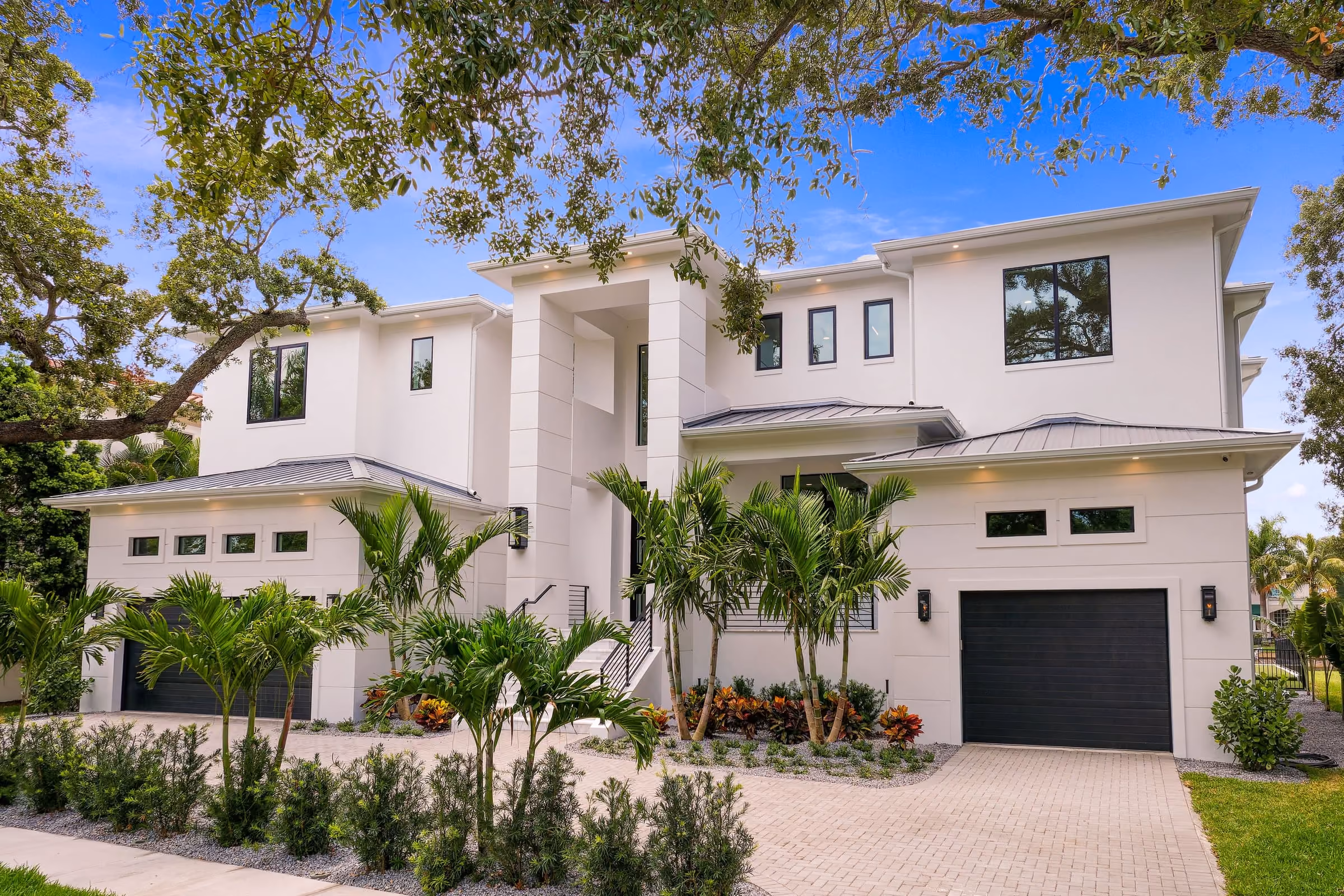Two-story white home with a paver drive, oak trees and a dark garage door