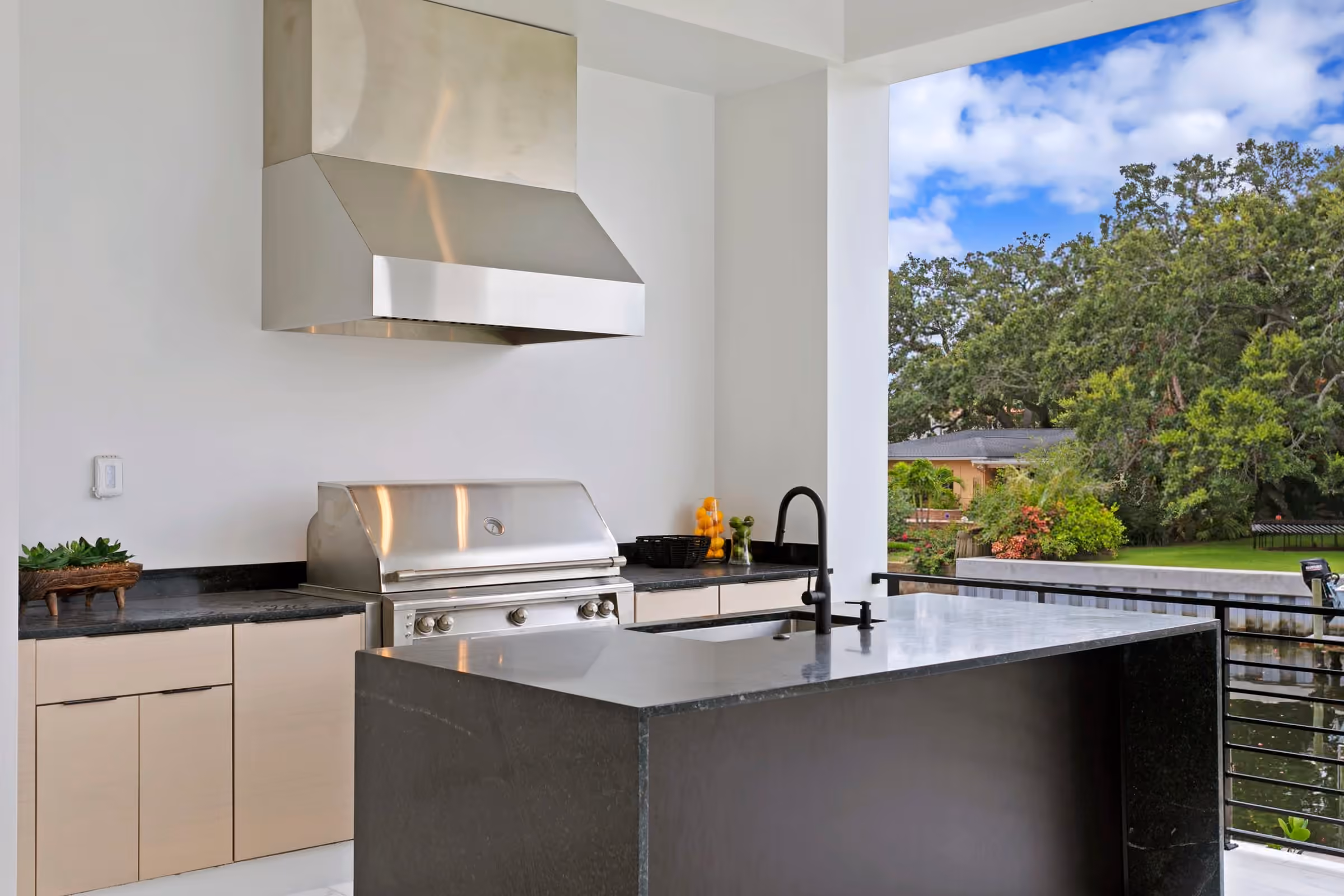 Outdoor kitchen with a grill and stainless hood under a covered balcony