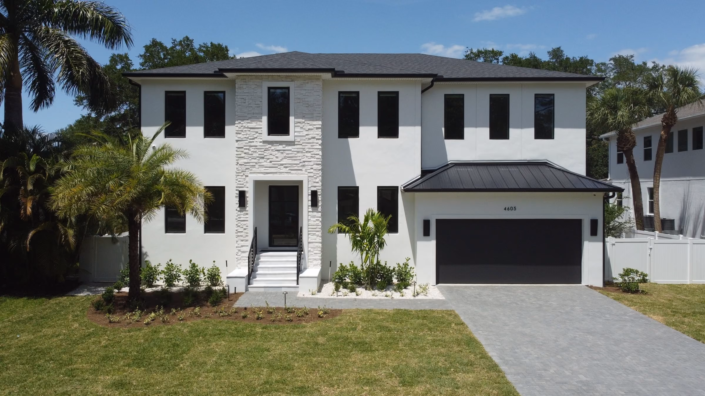 Two-story white home with a stone accent wall and a dark garage door
