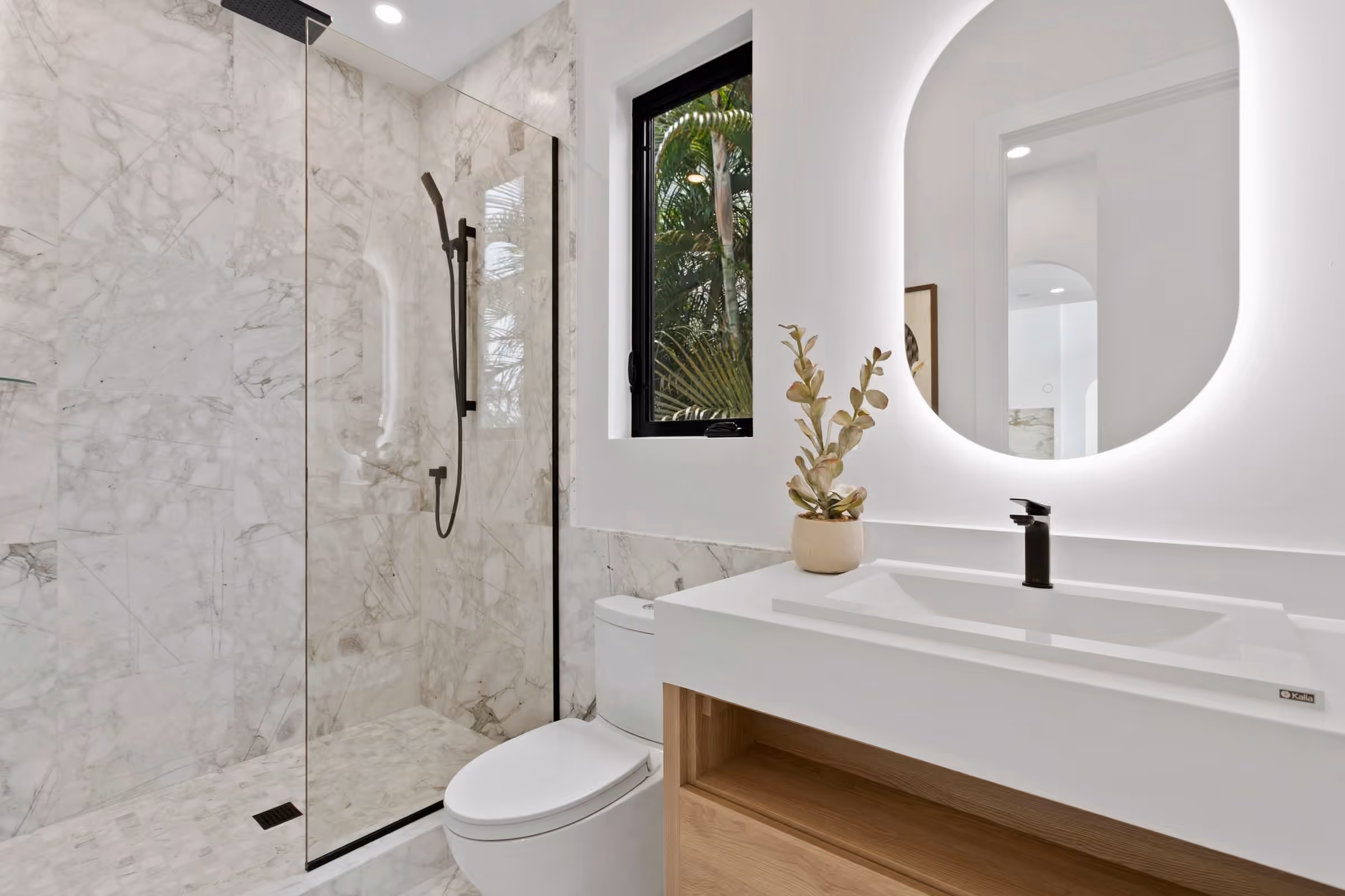 Bathroom with a marble shower, a backlit oval mirror and a floating oak vanity