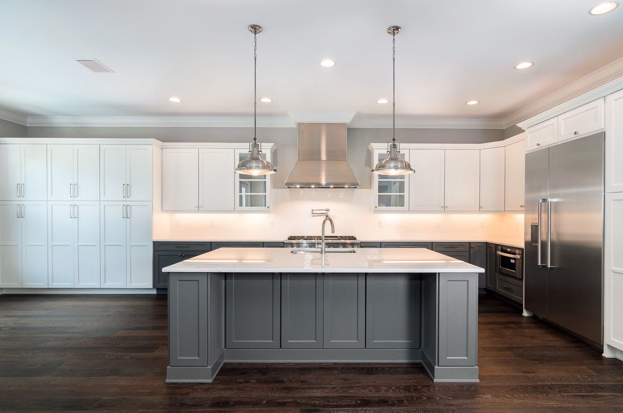 Kitchen with white cabinets, a gray island and pendant lights