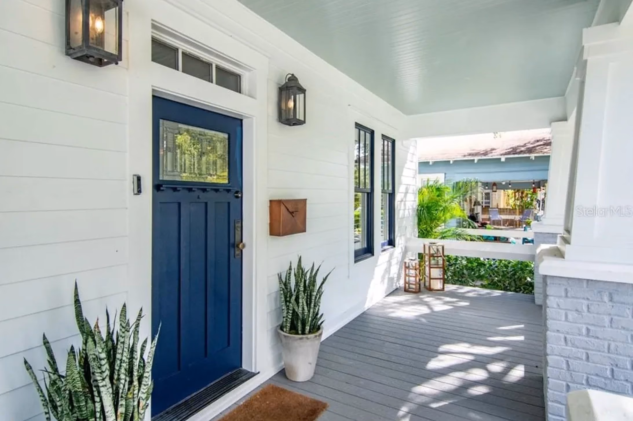 Front porch with a navy blue door, lanterns and potted plants